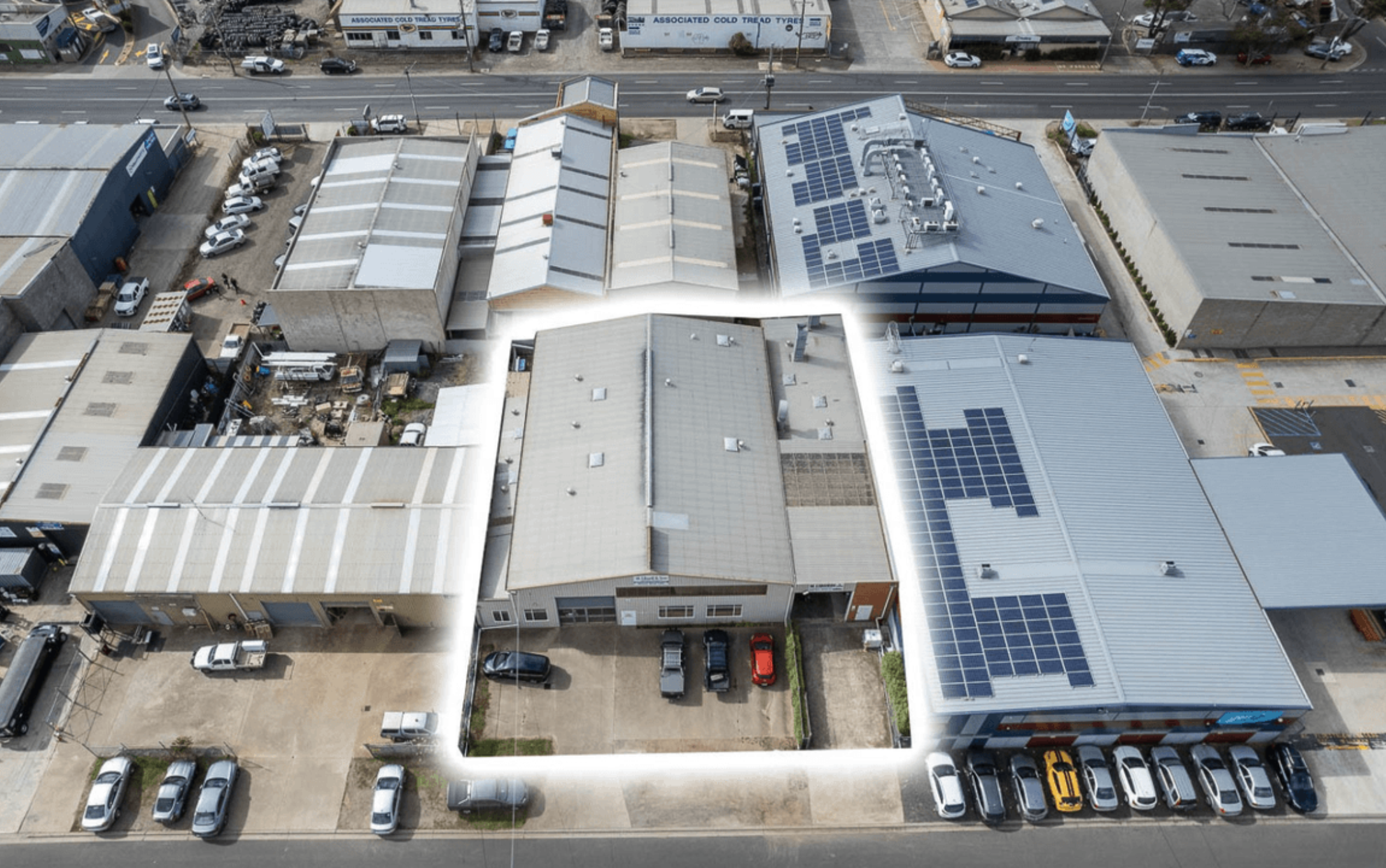 Aerial view of industrial area, multiple large sheds fill the space, a warehouse in the middle is the focus, it has a small carpark at the front with four cars parked in it, Shed is owned by Hamilton Group Geelong
